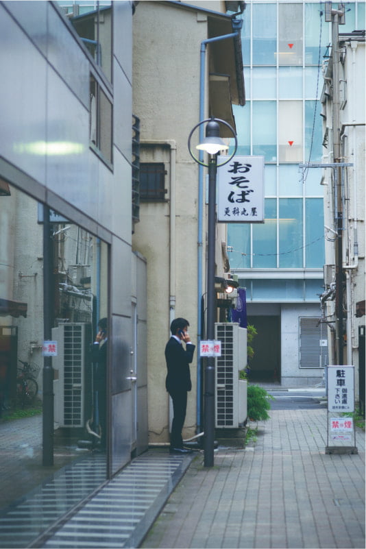 Photo of an office worker making a phone call in a back alley in Kyobashi